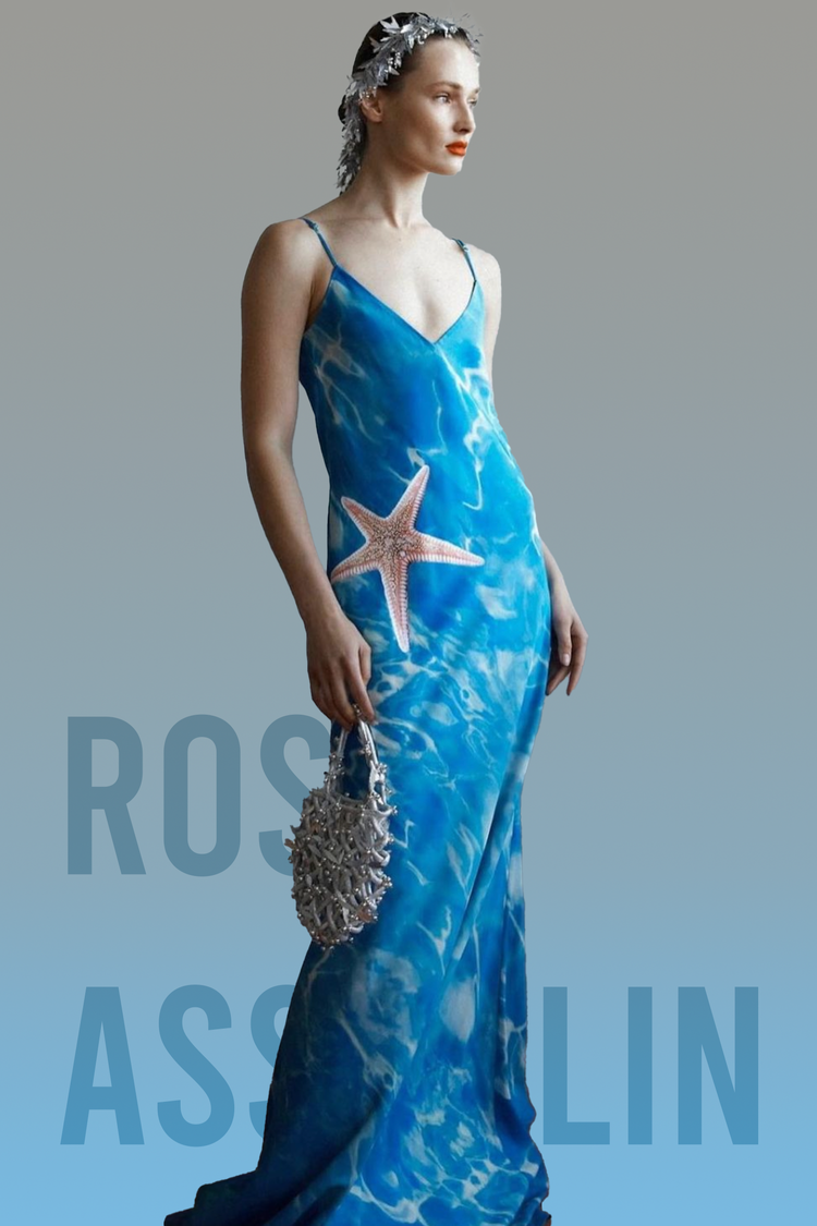 Woman in a silky blue gown with a pink starfish detail on the hip, holding a seashell-like textured bag.