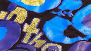 Close-up of a fabric with a vibrant blue and purple background and gold glitter text printed on the surface.
