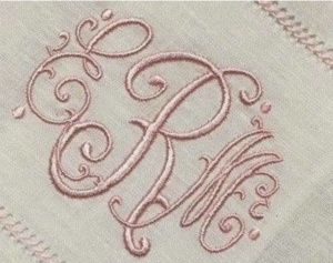 This is a delicate monogram embroidery design stitched in soft pink thread on a light-colored fabric, likely linen or cotton. The monogram appears to feature the intertwined initials E, R, and M, rendered in an elegant, ornate script style with flourishes, swirls, and teardrop accents. The overall aesthetic is classic and romantic, often seen on handkerchiefs, heirloom linens, or personalized gifts. The fine satin stitching and graceful curves give it a timeless, vintage charm — perfect for luxury embroidery or bespoke pieces.