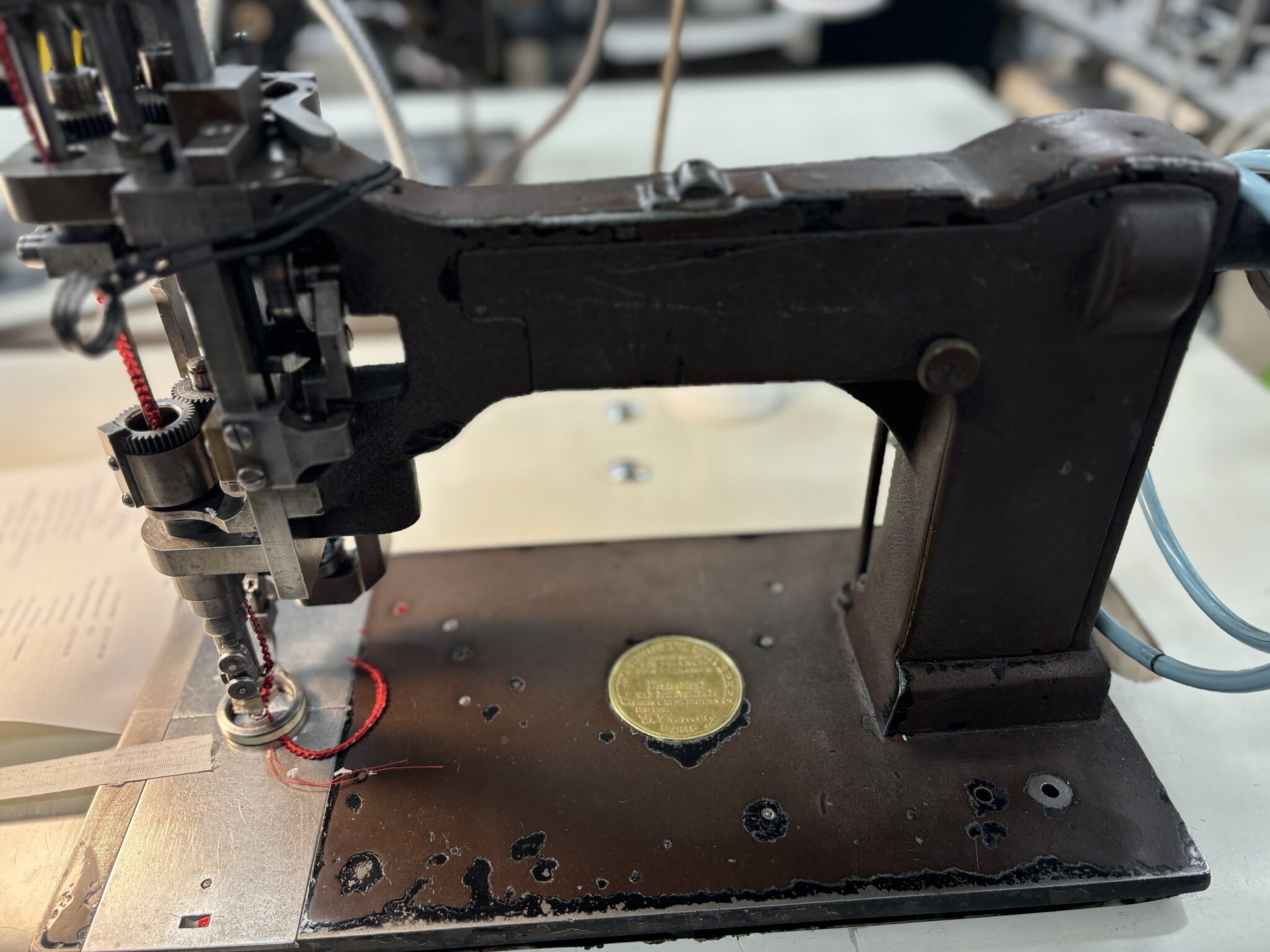 Close-up of a vintage chainstitch embroidery machine with exposed gears and a red thread running through the needle mechanism.
