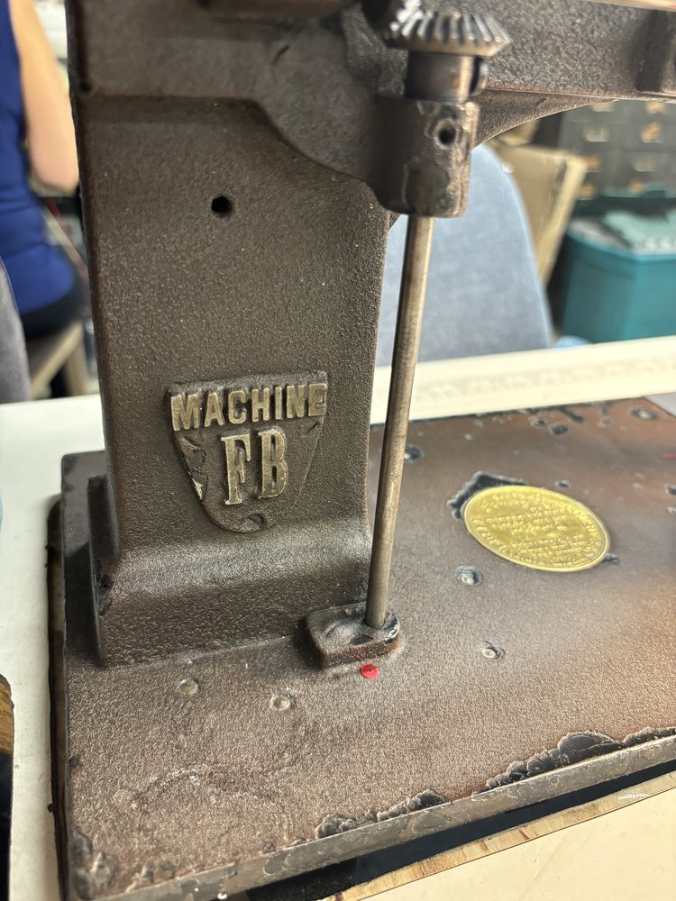 Close-up of an antique Cornely embroidery machine with “MACHINE FB” engraved on its cast iron frame.