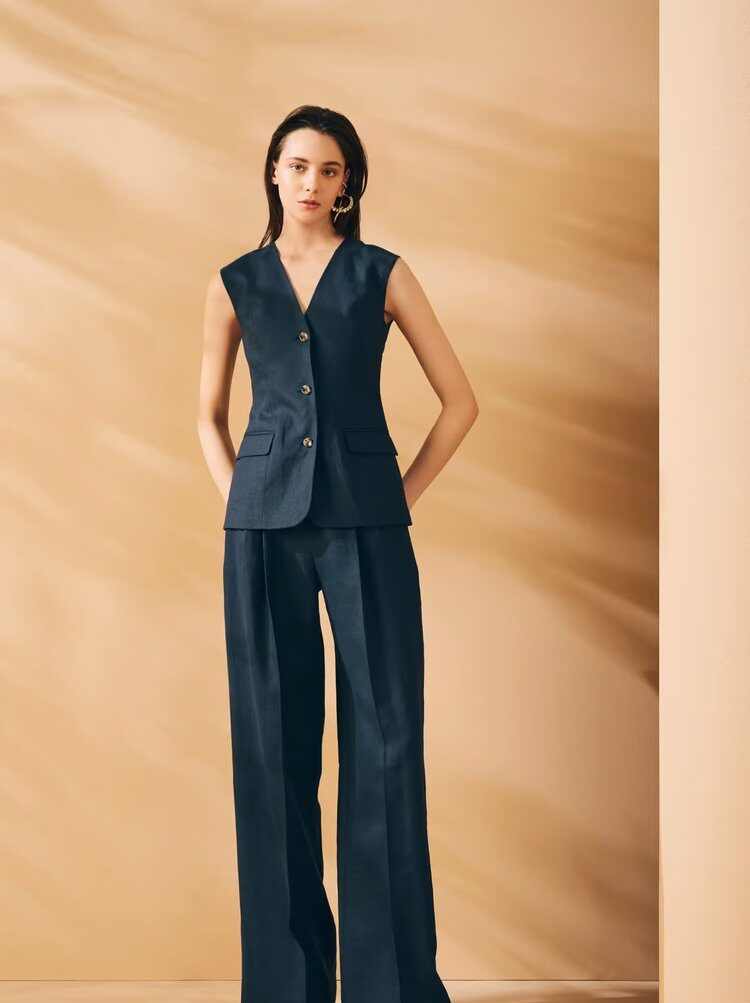 Woman wearing a sleeveless navy tailored vest and matching wide-leg trousers, posing against a soft beige background.