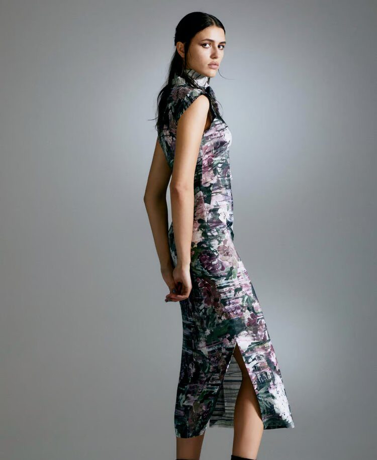 Woman in a fitted, floral-patterned dress with cap sleeves and side slit, posing against a gradient grey background.