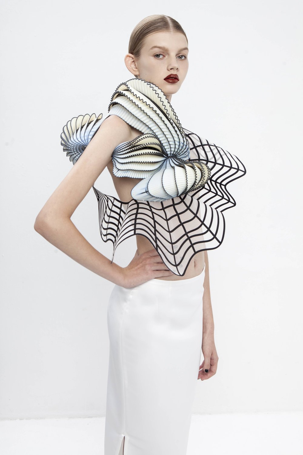 Model in a white skirt and a 3D sculptural top with black-edged, shell-like forms.