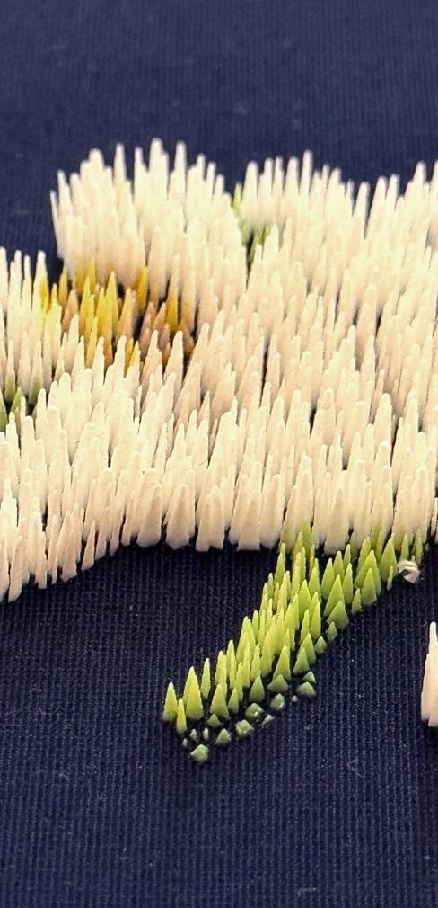 Close-up of textured embroidery in cream, yellow, and green threads on a dark navy background, resembling a brushstroke pattern.