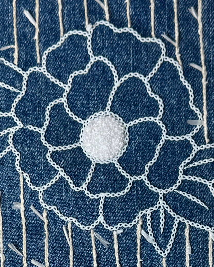Denim fabric embroidered with a large white floral outline and vertical sashiko-style stitch lines.