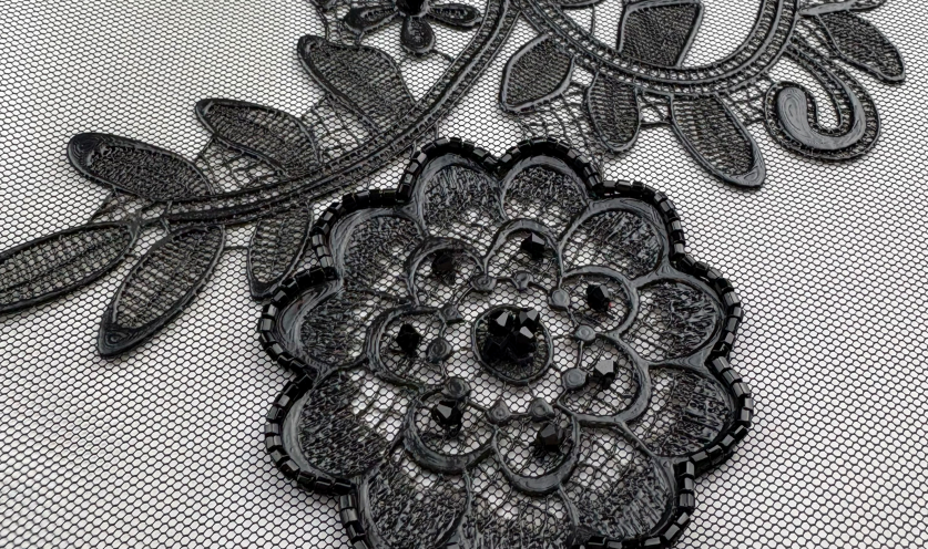Black floral lace embroidery with shiny accents layered over a fine mesh background.