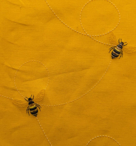 Yellow fabric embroidered with two small bees and dotted flight paths.