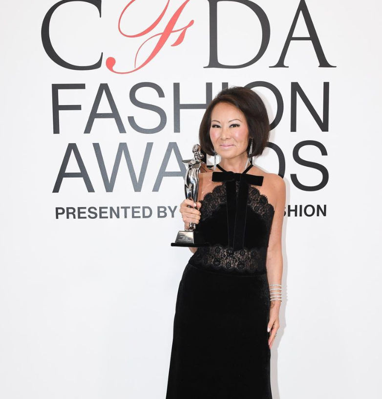 Woman in velvet gown holding CFDA trophy, smiling.