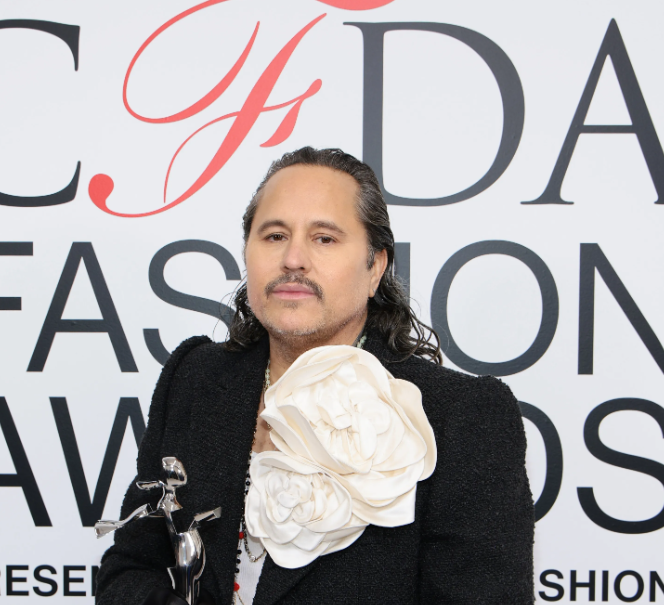 Man in black suit with oversized flower detail holding CFDA award.