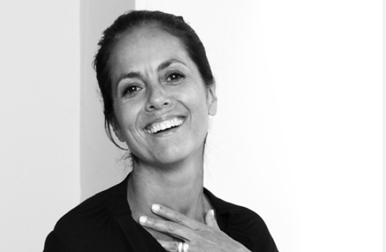 Smiling woman in monochrome shot, hand at collarbone.
