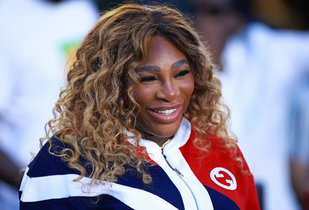 Serena Williams smiling in red, white, and navy sporty top.