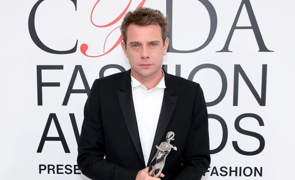 Man in tuxedo holding CFDA award in front of step-and-repeat.