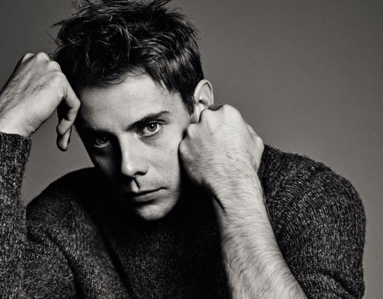 Man in black-and-white image staring intensely with hands near face.