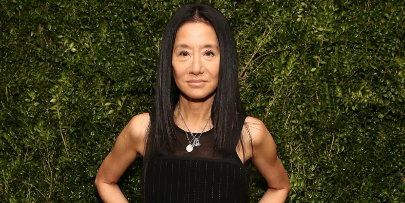 Vera Wang standing in front of a hedge wall wearing a black sleeveless dress.