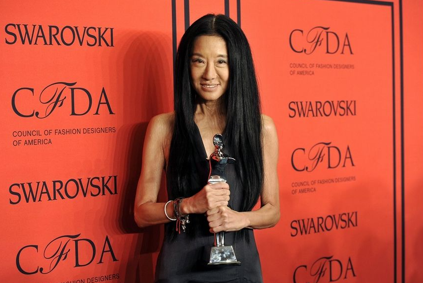 Vera Wang holding CFDA trophy in front of red backdrop.