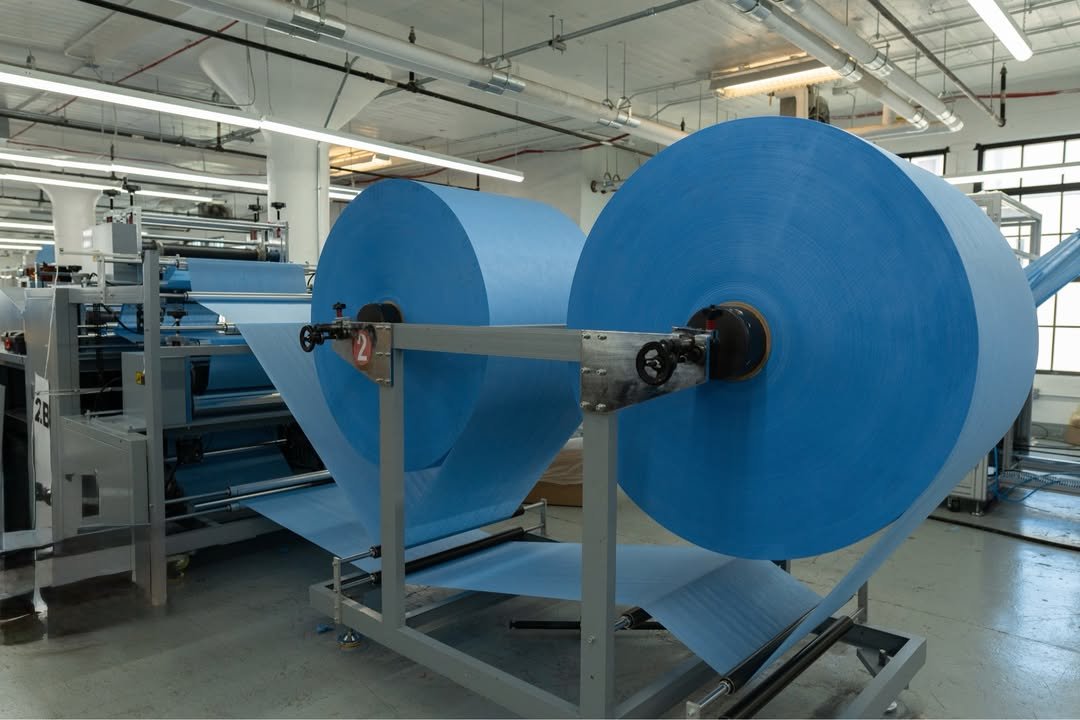 Two large blue fabric rolls mounted on a textile machine inside a well-lit manufacturing facility.