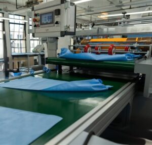 Textile machine laying out blue fabric sheets with automated rollers and cutting tools.