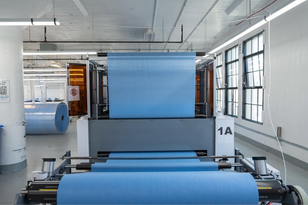 Blue textile roll being processed through a fabric spreading machine in a bright factory.