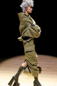Model in green deconstructed outerwear and platform boots walking on a wooden runway.
