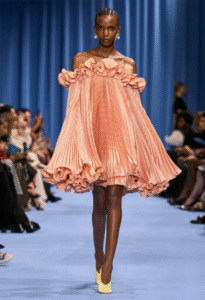 Model walks in a voluminous peach pleated mini dress with floral accents.