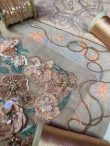 Embroidered floral tulle with threads and sequins arranged around it.