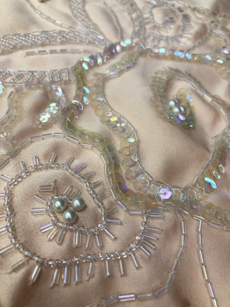 Close-up of shimmering beadwork and sequins on satin-like fabric.