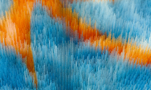 Close-up of a highly textured embroidery piece in vibrant orange, light blue, and dark blue threads, arranged in a directional, brushstroke-like pattern.