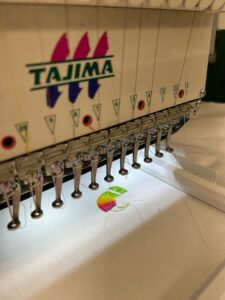 Tajima embroidery machine stitching a colorful logo onto white fabric.