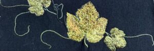 Glittery green leaf embroidery on dark fabric with curling vine details.