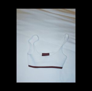 White cropped tank top with red logo trim laid on a bed