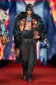 Male model in an oversized jacket with flame graphics, walking down a red runway
