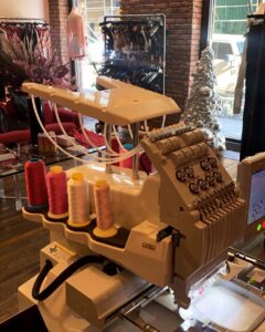 Embroidery machine with multiple pink and yellow thread cones in a showroom.