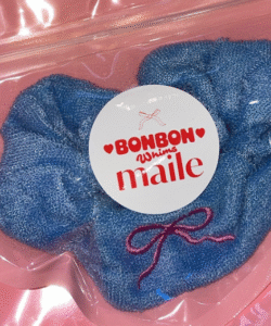 Close-up of blue denim scrunchie with embroidered bow, inside Bonbon Maile packaging.