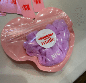 Pink heart-shaped packaging with a lavender scrunchie embroidered with “NIC.”