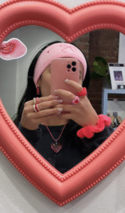 Girl taking a mirror selfie with pink accessories, framed by a heart-shaped mirror.