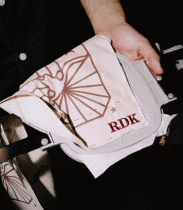 Hand holding a stitched fabric piece with a rose-brown line drawing and the initials “RDK”.