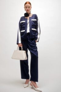 Woman wearing a navy blue and white color-blocked pantsuit with wide-leg trousers and a matching cropped jacket, holding a light beige handbag.