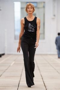 Model walking in a white lace pantsuit with a matching long shirt and a cropped graphic tank top that reads “MAMBA.”