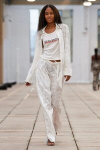 Model wearing a fitted black tank top with a subtle white graphic and slim black trousers on the runway.