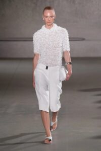 Model walking the runway in an all-white textured shirt and wide-leg shorts.