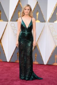 Woman in a dark green sequined gown with deep neckline on the Oscars red carpet.