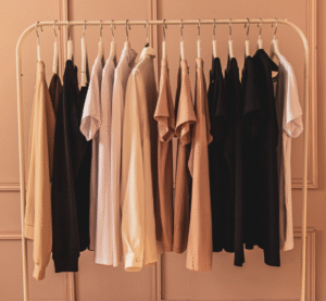 Rack of neutral-toned garments arranged by color in a soft pink room.