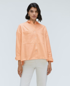 Woman wearing a loose, peach button-up shirt and white pants.