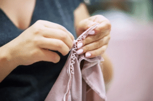 Hands carefully sewing pink fabric with a visible hand-stitching technique.