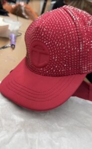 Close-up of a red baseball cap fully adorned with rhinestones and a raised embroidered logo.
