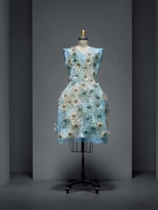 Blue embellished floral dress displayed on a mannequin in a dark exhibition room.