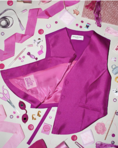 Pink satin Barbie vest opened to reveal its glossy lining, surrounded by sewing and fashion accessories in various shades of pink.