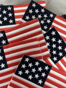 Close-up view of embroidered patches of the United States flag, layered atop one another.