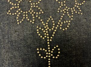 Golden floral embroidery stitched into black denim fabric.
